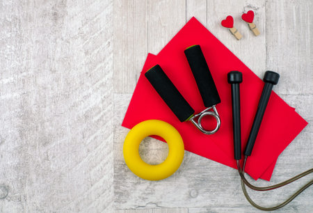 Fitness expanders, jump rope, red envelopes on gray wooden background. Love and sport concept. Top...