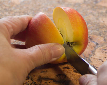 we hold a yellow-red apple in our hands and cut it into two halves with a knife, making dessertの写真素材