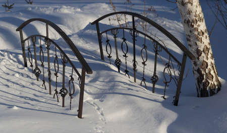 a metal bridge with forged fragments in the snow, an element of landscape design, a park in winter, a walking area in the winter seasonの写真素材