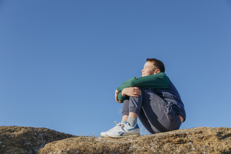 Portrait of a boy sitting on a rock against the blue skyの写真素材