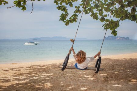 Girl sitting on the swing on the tropical beach, paradise islandの写真素材
