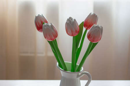 Bouquet of red and white wooden tulips in a white jug against the window and delicate tulleの写真素材