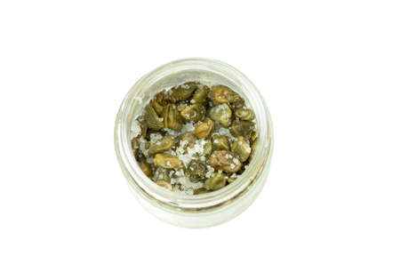 Green capers with coarse salt in a glass jar isolated on white background, top view. Salty vegetables spice seasoning, culinary ingredientの写真素材