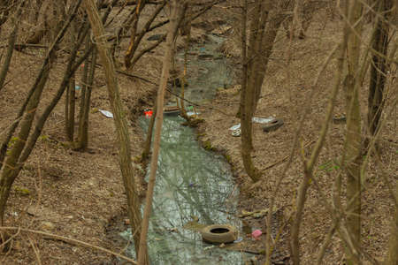 Spring forest stream river garbage waste plastic tire glass bottles after the snow melted. Environmental issues, planet pollution, garbage collection waste sorting recyclingの写真素材