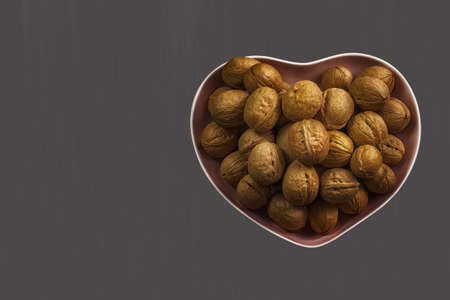 Inshell walnuts in a heart-shaped plate, copy space. Whole ripe walnut, healthy food for the heart and brain. Vegetable Protein Vegetarian vegan vegetable protein. Gray backgroundの写真素材