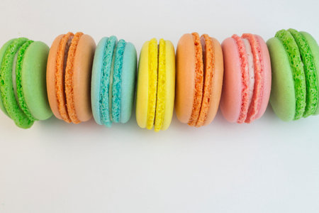 Multicolored macaroni biscuits on a white background close-up. Green blue red yellow macaroni laid out horizontally, sweet pastry dessert rainbow color. Holiday pastries, sweet pastry cookies, tea cakeの写真素材