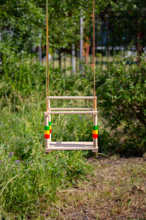 Children's wooden swing on the ropes hang on the background of park greenery, vertical no peopleの写真素材