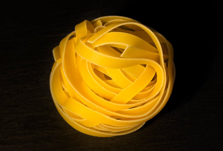 Uncooked tagliatelle pasta on a black background. A ball of lump of pasta noodles on a black background, top viewの写真素材