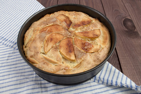 Apple pie homemade in a baking dish on a wooden table with a blue striped napkin. Pie with apples, slices of apples are on the surface, sweet pastriesの写真素材