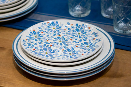 A stack of different blue plates with flowers with a strip on a wooden table with a blue napkin....