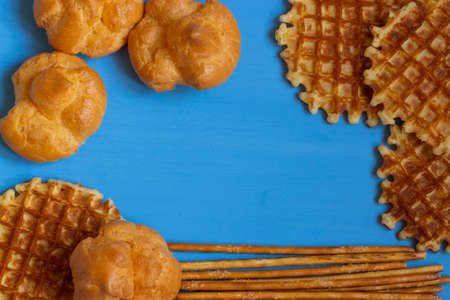 A frame of sweets, blue wooden background framed in profiteroles, Viennese waffles and sugar straws. Sweet life, copy space. Greeting card background congratulation Postcardの写真素材