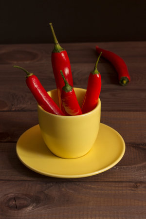 Red hot caen chili pepper, a few fire peppers, food seasoning, caen pepper in a yellow cup on a wooden table, low keyの写真素材