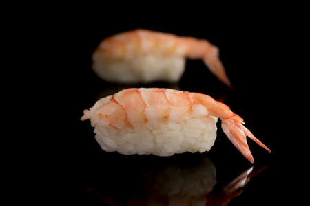 Sushi with fresh pink langoustine shrimp, mini lobster with a tail on a black background reflection. Japanese cuisine is a dish of rice and raw seafoodの写真素材