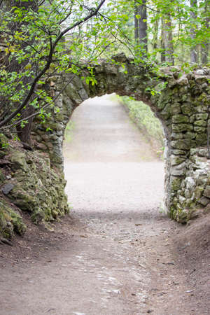 Stone arch surrounded by foliage of trees. Beautiful arch of rough bricks, secret passage in the park, verticalの写真素材