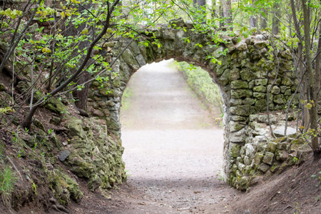 ancient stone arch overgrown with moss. Path leading to stone wall opening from rough old stone,...