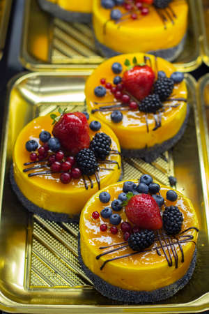 Mango-style souffle round biscuit mini cakes on a cafe window. Decor made from strawberries, currants, blueberries and blackberries.の写真素材