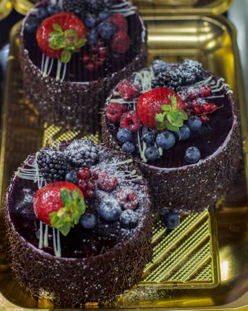 Chocolate cakes on a pastry shop window, round chocolate cake with berries, raspberries, blackberries, blackberries, blueberries, currants and powdered sugarの写真素材