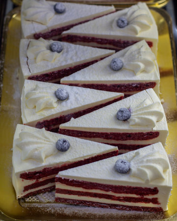 A triangular piece of blueberry berry cake with vanilla cream. Pieces of cake with red white layers decorated with blueberry blueberries and cream curlsの写真素材