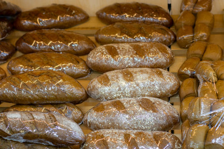 Loafs of fresh rye bread in flour sprinkles wrapped in plastic film on a bakery counter, a palette with fresh breadの写真素材