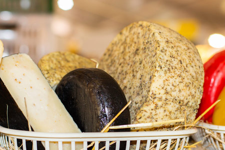 Different varieties of cheese in a basket on a farm counter. Round cheese head with spices, background wallpaper horizontalの写真素材