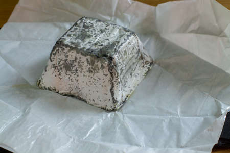 Soft farm cheese made from goat milk with mold and charcoal. Briquette pyramid parallelepiped a piece of cheese in white paper close-upの写真素材