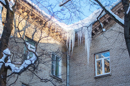 Big long icicles hanging from the roof of a residential building, winter ice cold snow nature. Freezing ice water at the corner of a brick apartment building, dangerの写真素材