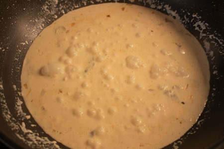 Creamy mushroom sauce is boiling in a black frying pan. Bubbles are boiled white sauce, cream cheese mushrooms onions, dressing for meat dishes. Cooking creamy mushroom sauce at homeの写真素材