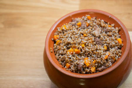 Buckwheat with carrots and meat baked in a clay pot on a wooden table. Buckwheat porridge with meat and vegetables cooked in potteryの写真素材