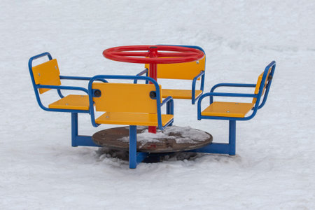 Empty playground in winter, cold weather, low temperature, swing yellow red blue metal multicolored funny mini carousel. Lots of white snow with traces no peopleの写真素材