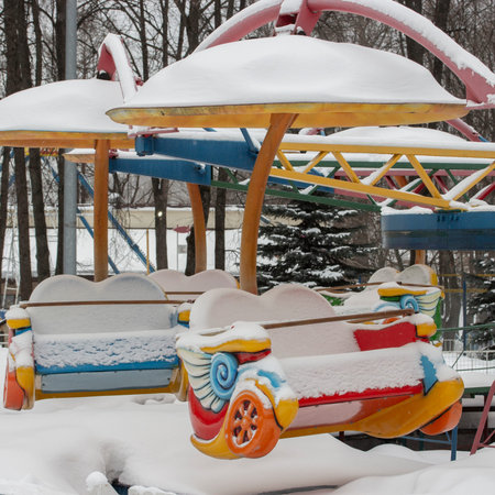 Swing carousel seat in the snow, bright multi-colored attraction empty hidden under the snow, winter amusement parkの写真素材