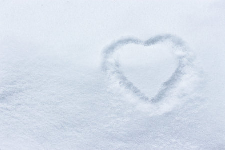 Heart in the snow, hands drawing on a clean empty snow surface, winter cold. Concept of love, romantic relationship, love message winter outdoorsの写真素材