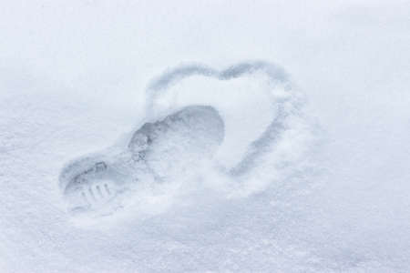 Heart drawing in the snow. Footprint from the boot and silhouette of the heart. Winter concept broken heart, unhappy love, breakup coldness dislikeの写真素材