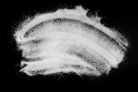 A pile of sugar sprinkled on a black background, backdrop. Abstract sprinkle of white refined sugar granules. Design elementの写真素材