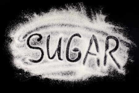 Word sugar, hand lettering on black background. The text is written on a pile of powdered white granulated sugar. Sugar eating harm conceptの写真素材