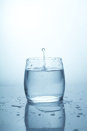A splash of water in a glass, a drop of water hanging in the air, pure drinking spring clear water, a splash with a drop of water in a glass gobletの写真素材