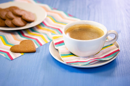 White cup of coffee with cookies on a blue table with striped napkins. Morning black hot coffee with homemade sweet pastries, heart-shaped gingerbread cookiesの写真素材