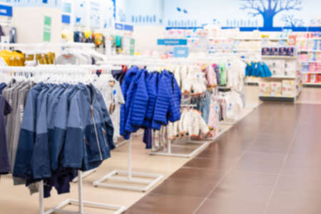 Defocus background, children's clothing store and goods for children. Jackets and windcheaters on hangers, even rows of textile products, perspectivity blurred backdrop for sales design.の写真素材