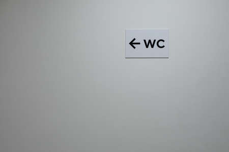 White plastered wall with WC sign and arrow pointer. Empty clean wall with a pointing sign, passage to the toilet. Sign indicating the location of the hygienic room, toilet WCの写真素材