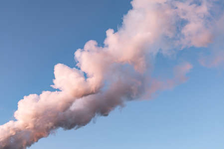 White pink smoke vapor against a clear blue sky. The smoke from the chimney at sunset painted in pink. Air pollution, atmosphere. One smoke for designの写真素材