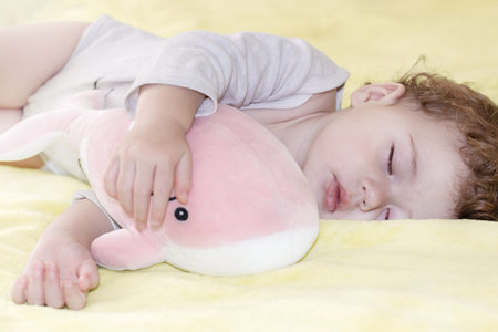Little girl sleeping boy hugging a toy pink whale. Little Caucasian child sleeps with a soft toy,...