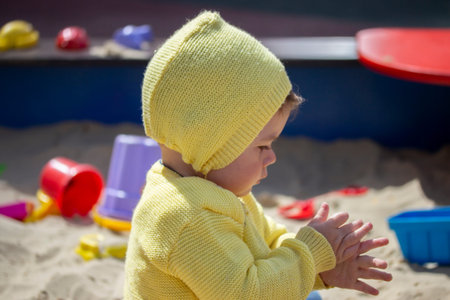 European child girl boy shakes his hands from the sand in the sandbox. Child baby one year old...