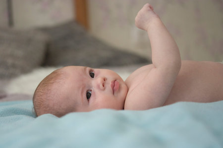 A three-month baby kid lies on his back with his arms raised. Newborn baby is studying his hands....