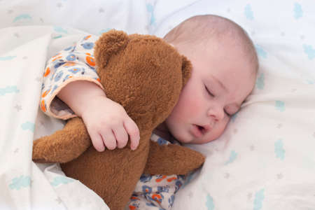 The half-year baby kid sleeps around with a teddy bear. Portrait of a cute sleeping baby, plump lips, snub nose. Portrait close-up soft focusの写真素材