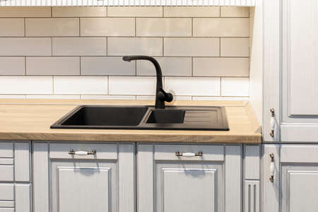 Black stone sink and faucet in the kitchen. White facade kitchen furniture made of natural wood, oak table top. Kitchen interior design, finishing in light colorsの写真素材