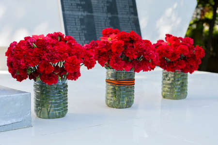Three bouquets of red clove pink at the monument to the soldiers who died in World War II, the St George ribbon is a symbol of memory and prideの写真素材