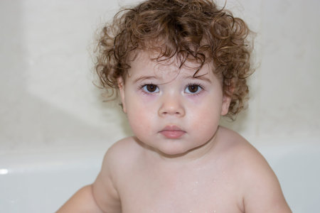 Little caucasian girl 1 year old takes a bath, wet face of a curly toddler close-up