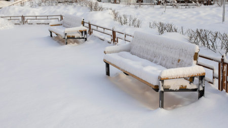 Snow-covered bench sunk in the snow, a large amount of precipitation in winter, snowfall in the cityの写真素材