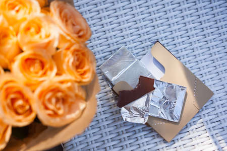 Orange roses, chocolate bar in metal foil on tableの写真素材