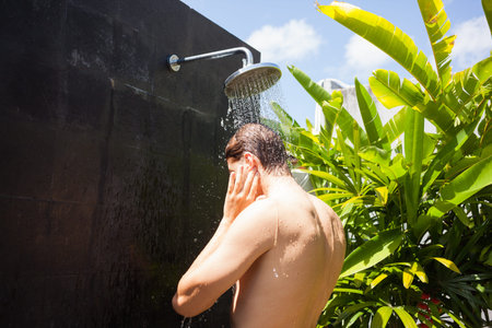 Man washing ears while taking shower on sunny day.