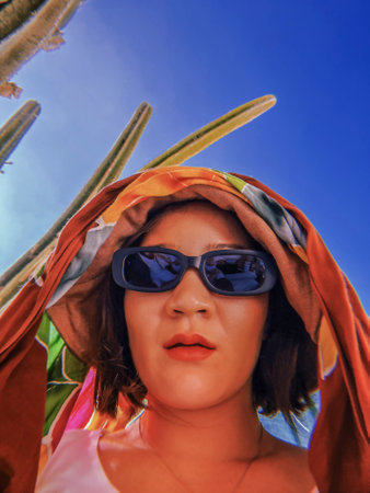 Female traveler wearing sunglasses against blue sky with cacti. Travel Mexico. Korean woman on a trip to desert. Thirty tired girl. Soft focus. film grain pixel texture. Defocused.の写真素材